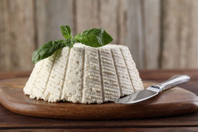 Photo of Tasty ricotta (cream cheese), basil and knife on wooden table, closeup