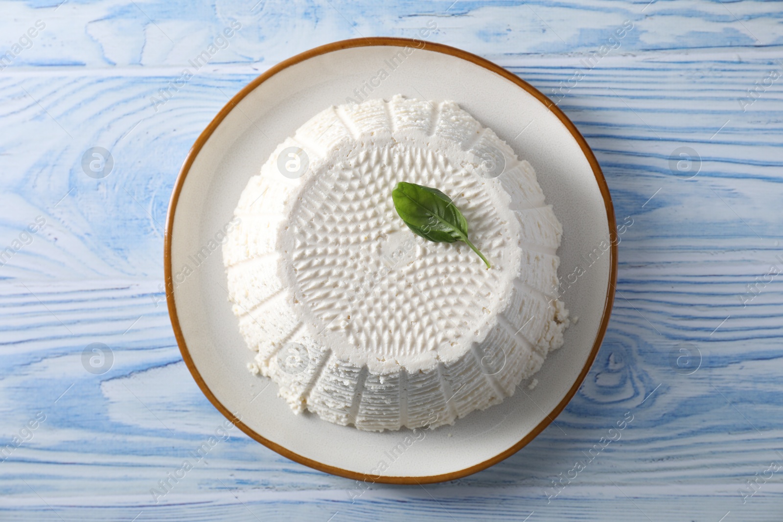 Photo of Tasty ricotta (cream cheese) on light blue wooden table, top view