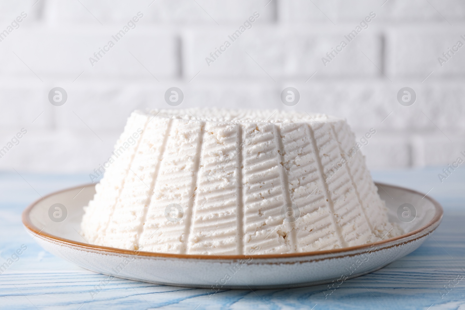 Photo of Tasty ricotta (cream cheese) on light blue wooden table, closeup