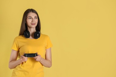 Woman playing video games with controller on yellow background, space for text