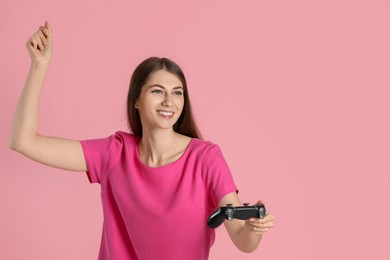 Happy woman playing video games with controller on pink background, space for text