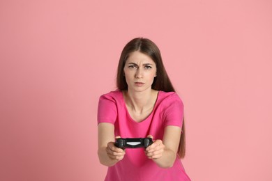 Woman playing video games with controller on pink background