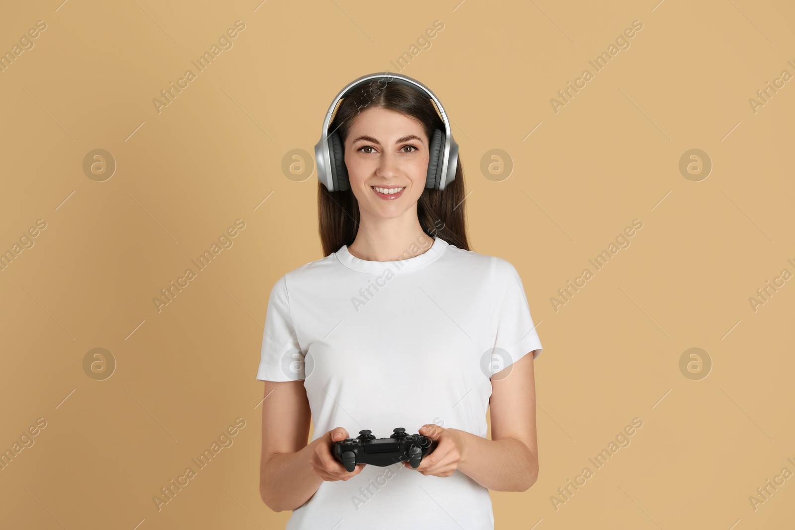 Photo of Happy woman in headphones playing video games with controller on beige background