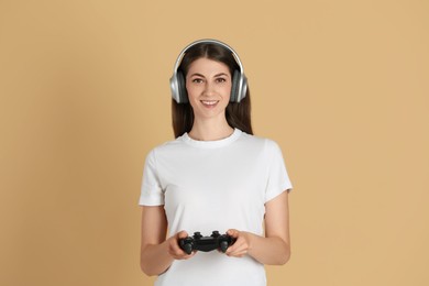 Happy woman in headphones playing video games with controller on beige background