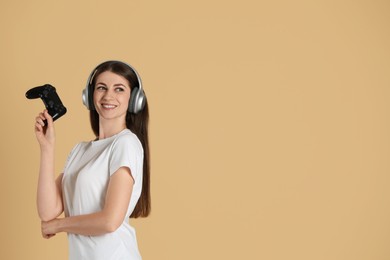 Happy woman in headphones with controller on beige background, space for text