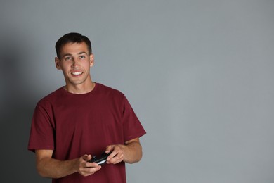 Happy man with controller on gray background, space for text