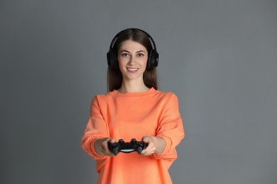 Photo of Happy woman in headphones with controller on gray background