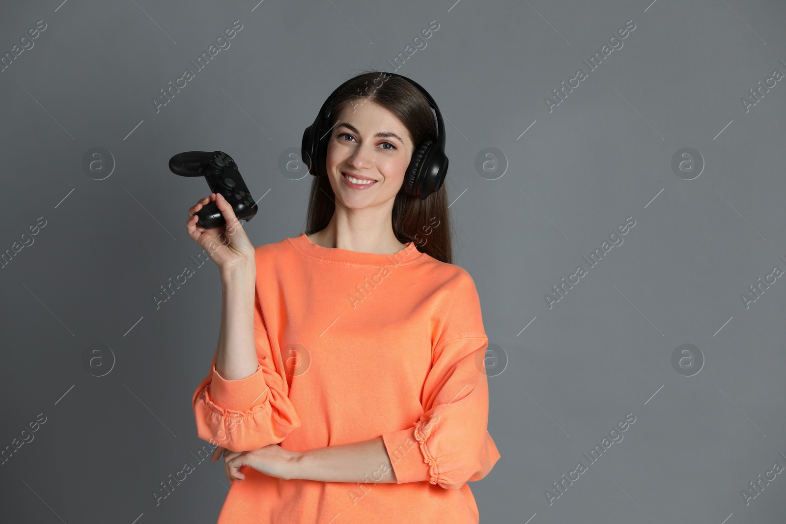 Photo of Happy woman in headphones with controller on gray background, space for text