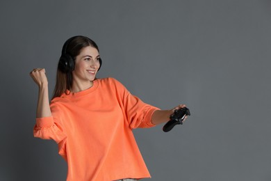 Happy woman in headphones playing video games with controller on gray background, space for text