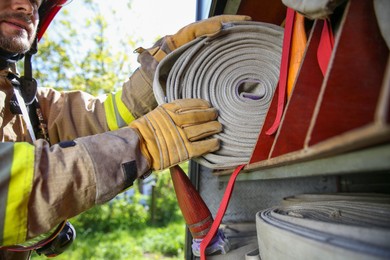 Photo of Firefighter in uniform with fire hose near truck outdoors, closeup
