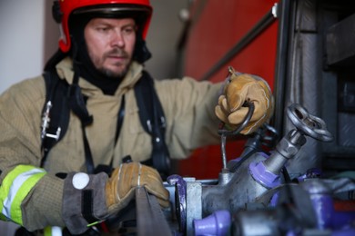 Firefighter in uniform with fire engine equipment at station, selective focus