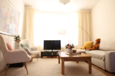 Cozy living room with modern furniture, TV set and bouquets of flowers, blurred view. Interior design