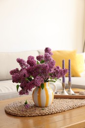 Photo of Beautiful fragrant lilac flowers in vase and candles on table at home