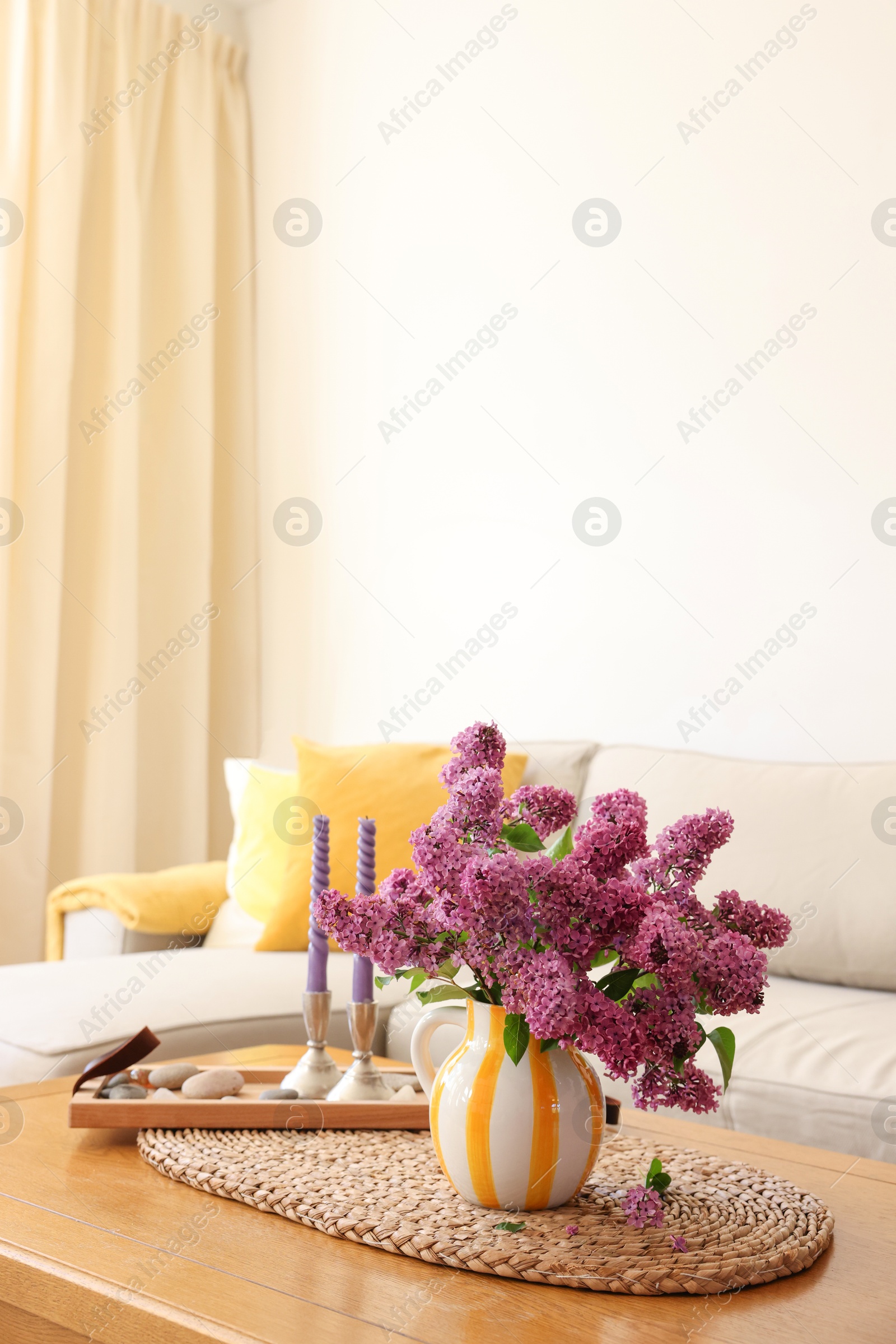 Photo of Beautiful fragrant lilac flowers in vase and candles on table at home. Space for text