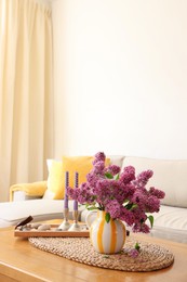 Photo of Beautiful fragrant lilac flowers in vase and candles on table at home. Space for text