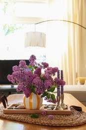 Photo of Beautiful lilac flowers in vase and candles on table at home