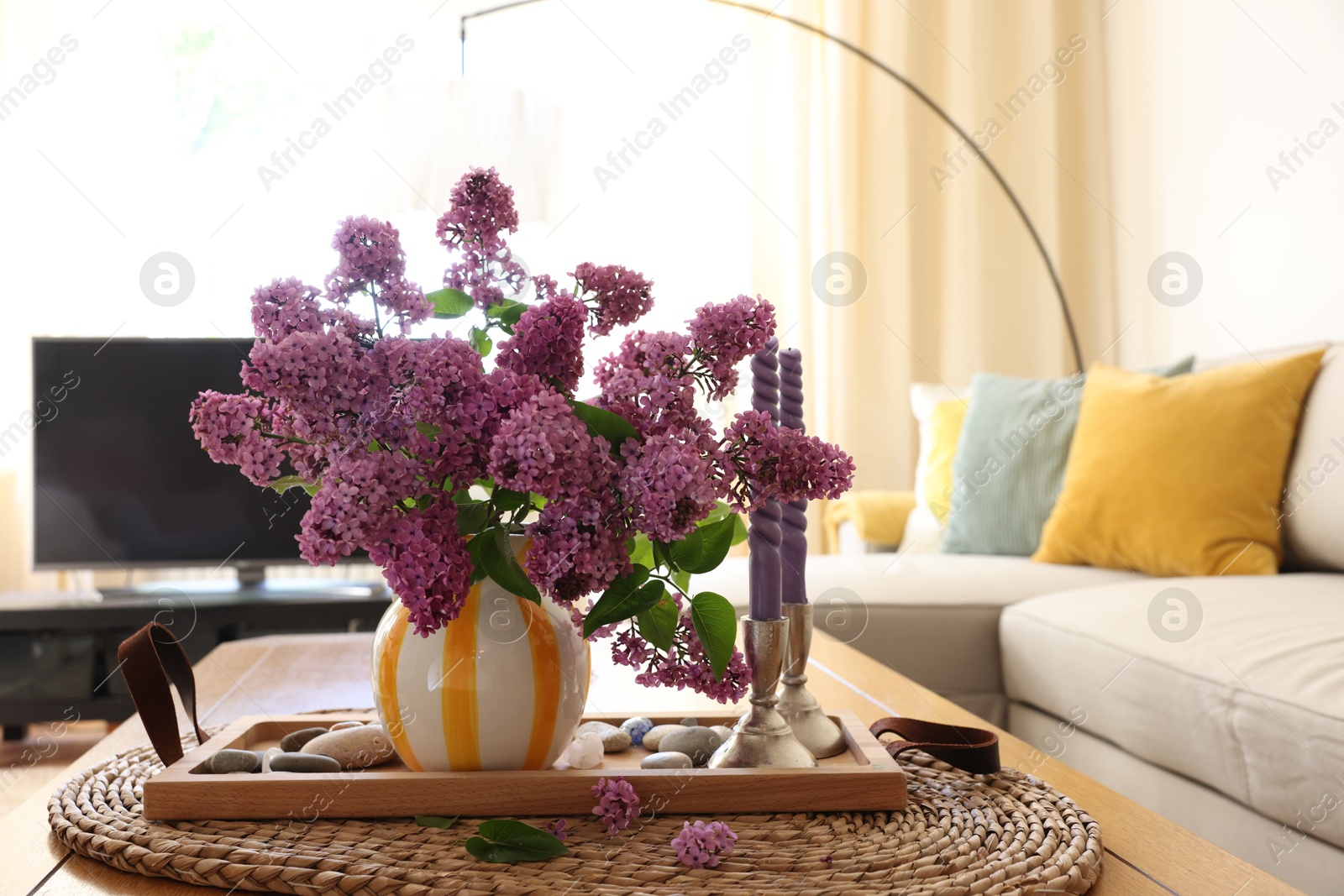 Photo of Beautiful lilac flowers in vase and candles on table at home. Space for text