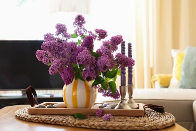 Photo of Beautiful lilac flowers in vase and candles on table at home