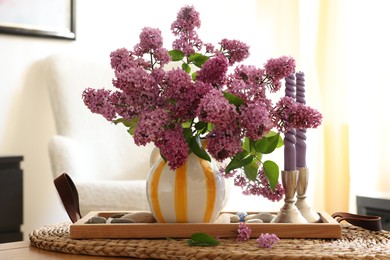 Photo of Beautiful lilac flowers in vase and candles on table at home