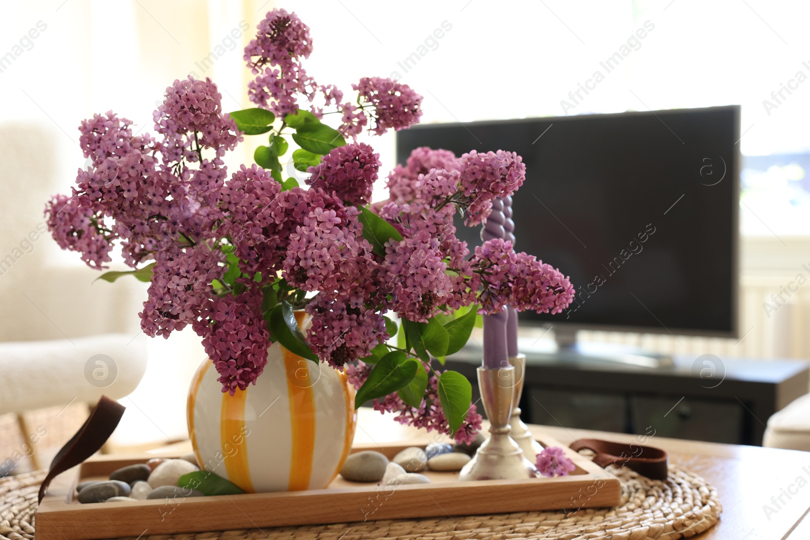 Photo of Beautiful lilac flowers in vase and candles on table at home