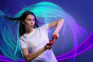 Image of Excited woman playing video game with controller on blue background. Bright lights around her