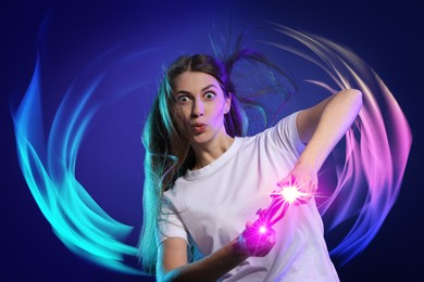 Image of Excited woman playing video game with controller on blue background. Bright lights around her