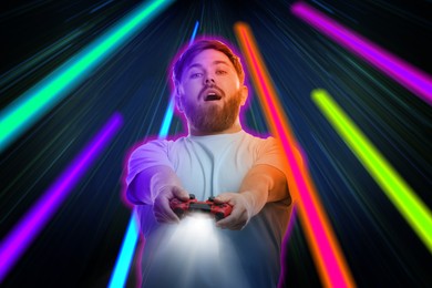 Excited man playing video game with controller on dark background. Bright light traces, motion blur effect