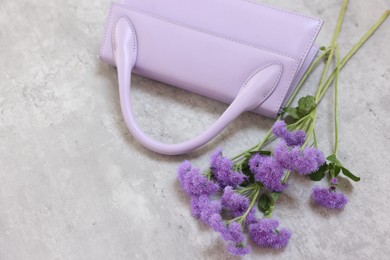 Photo of Stylish violet bag and ageratum flowers on gray textured table, above view