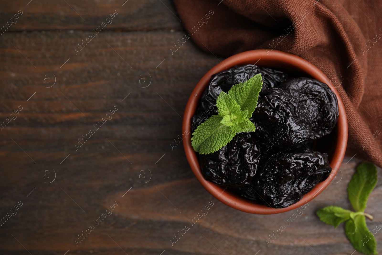 Photo of Tasty dried plums (prunes) and mint in bowl on wooden table, top view. Space for text