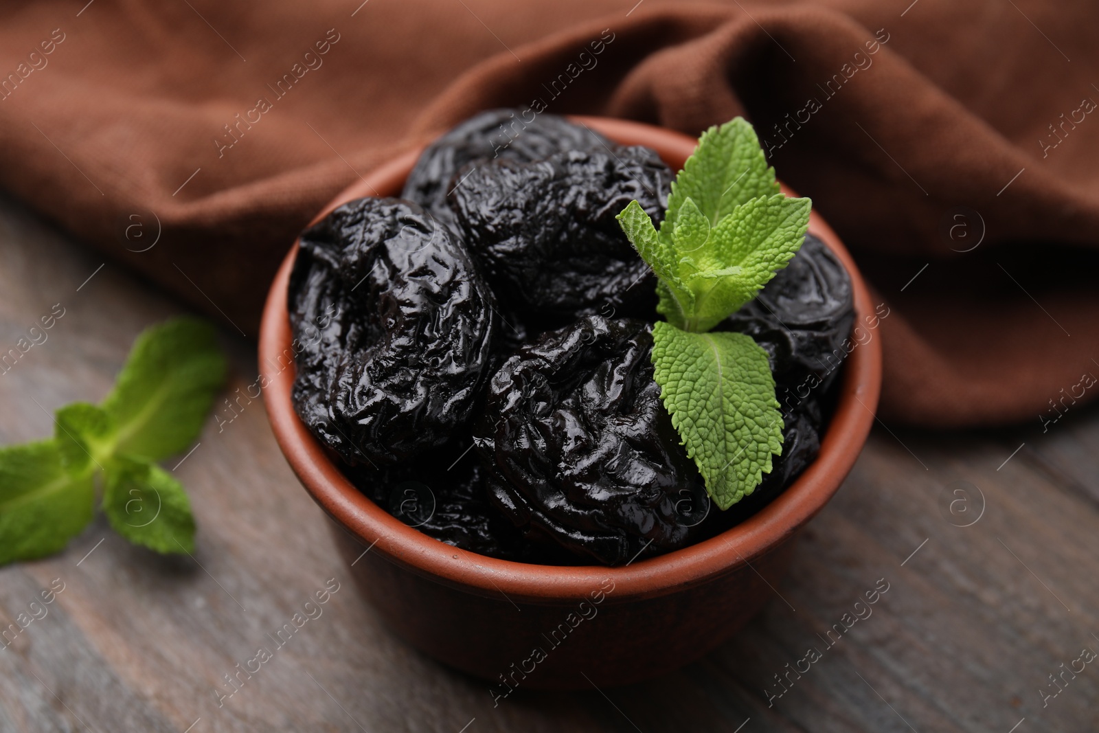 Photo of Tasty dried plums (prunes) and mint in bowl on wooden table, closeup