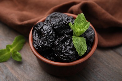 Photo of Tasty dried plums (prunes) and mint in bowl on wooden table, closeup