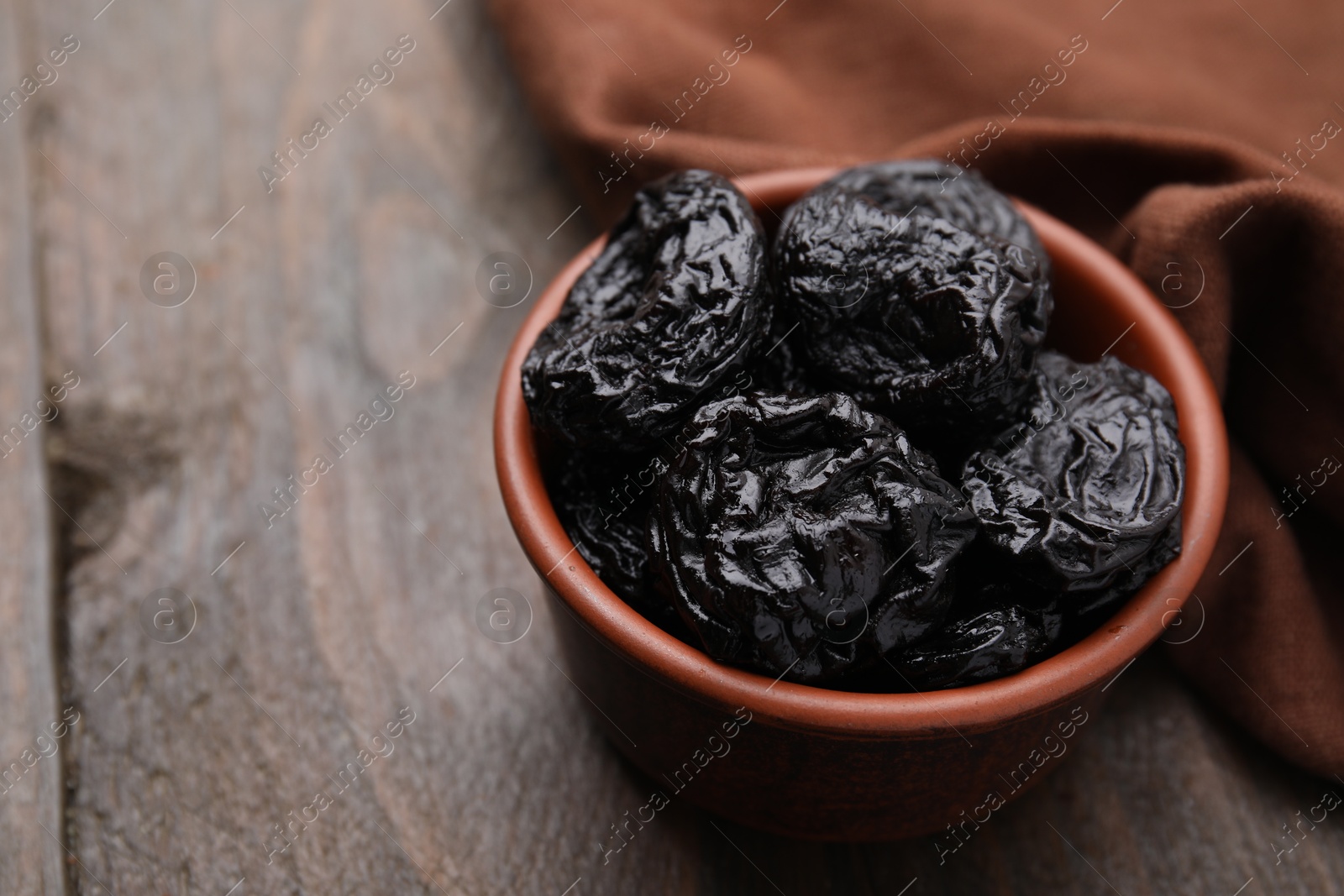 Photo of Tasty dried plums (prunes) in bowl on wooden table, closeup. Space for text