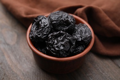 Photo of Tasty dried plums (prunes) in bowl on wooden table, closeup