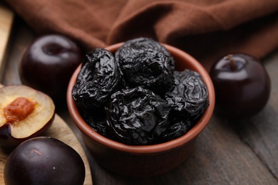 Photo of Delicious prunes in bowl and fresh ripe plums on wooden table, closeup