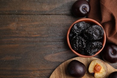 Delicious prunes in bowl and fresh ripe plums on wooden table, flat lay. Space for text