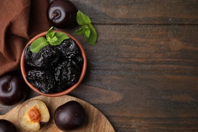 Delicious prunes with mint in bowl and fresh ripe plums on wooden table, flat lay. Space for text