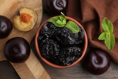 Delicious prunes with mint in bowl and fresh ripe plums on wooden table, flat lay