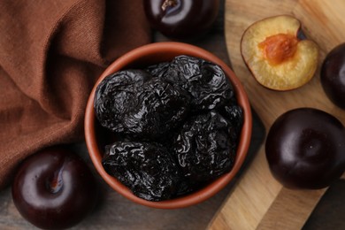 Delicious prunes in bowl and fresh ripe plums on wooden table, flat lay