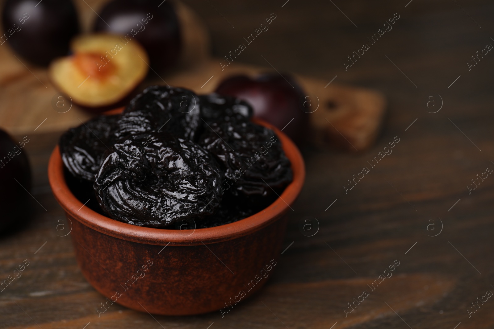 Photo of Tasty dried plums (prunes) in bowl on wooden table, closeup. Space for text