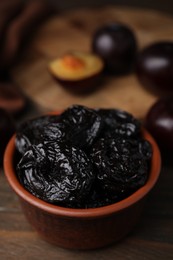 Tasty dried plums (prunes) in bowl on wooden table, closeup