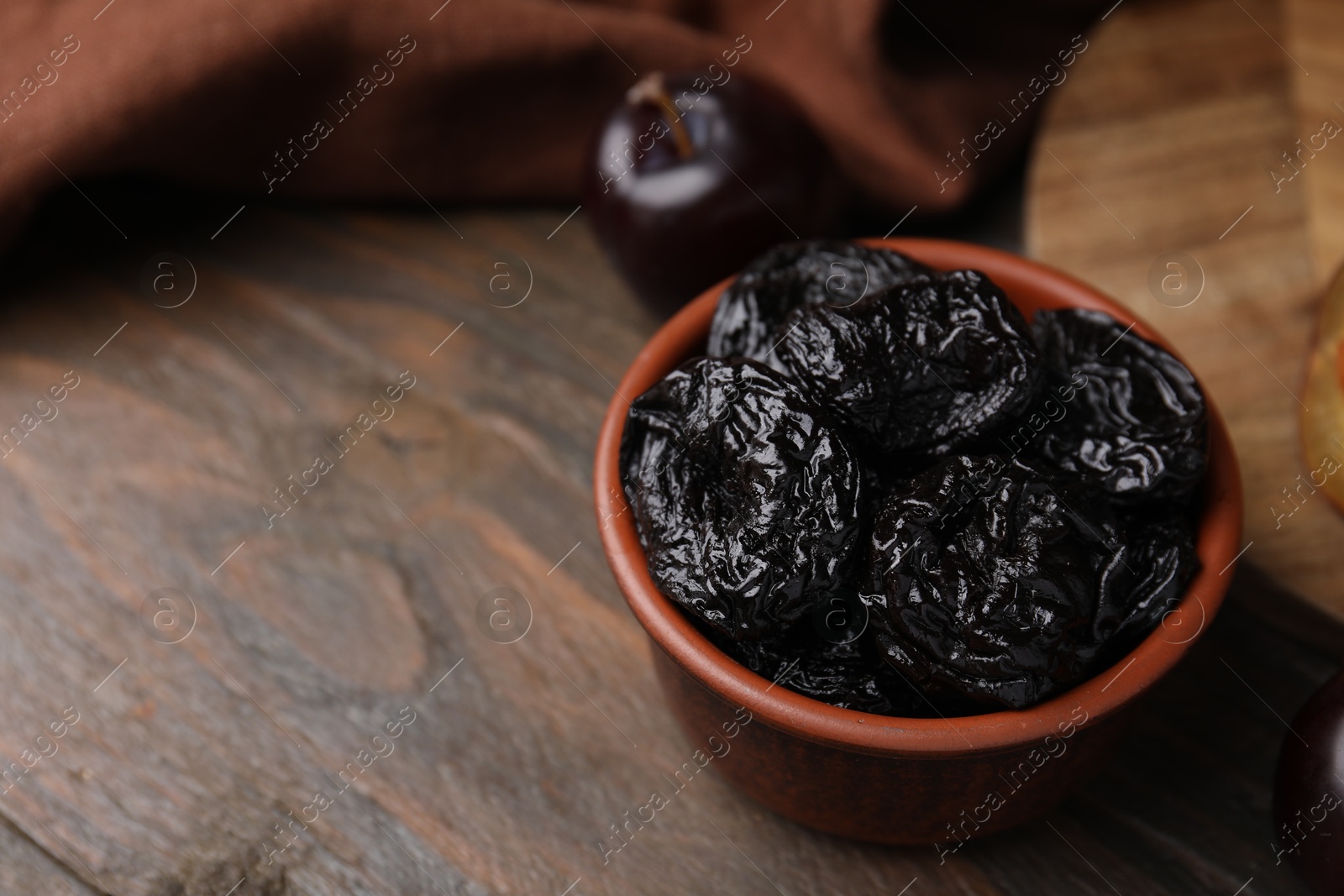 Photo of Tasty dried plums (prunes) in bowl on wooden table, closeup. Space for text