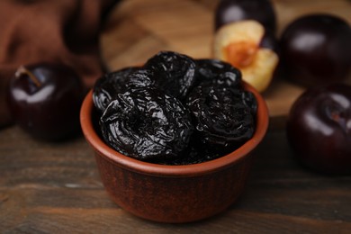 Photo of Tasty dried plums (prunes) in bowl on wooden table, closeup