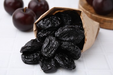 Photo of Paper bag with delicious prunes and fresh ripe plums on white tiled table, closeup