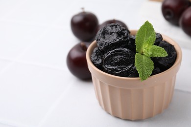 Delicious prunes with mint in bowl and fresh ripe plums on white table, closeup. Space for text