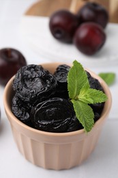 Photo of Tasty dried plums (prunes) and mint in bowl on white table, closeup