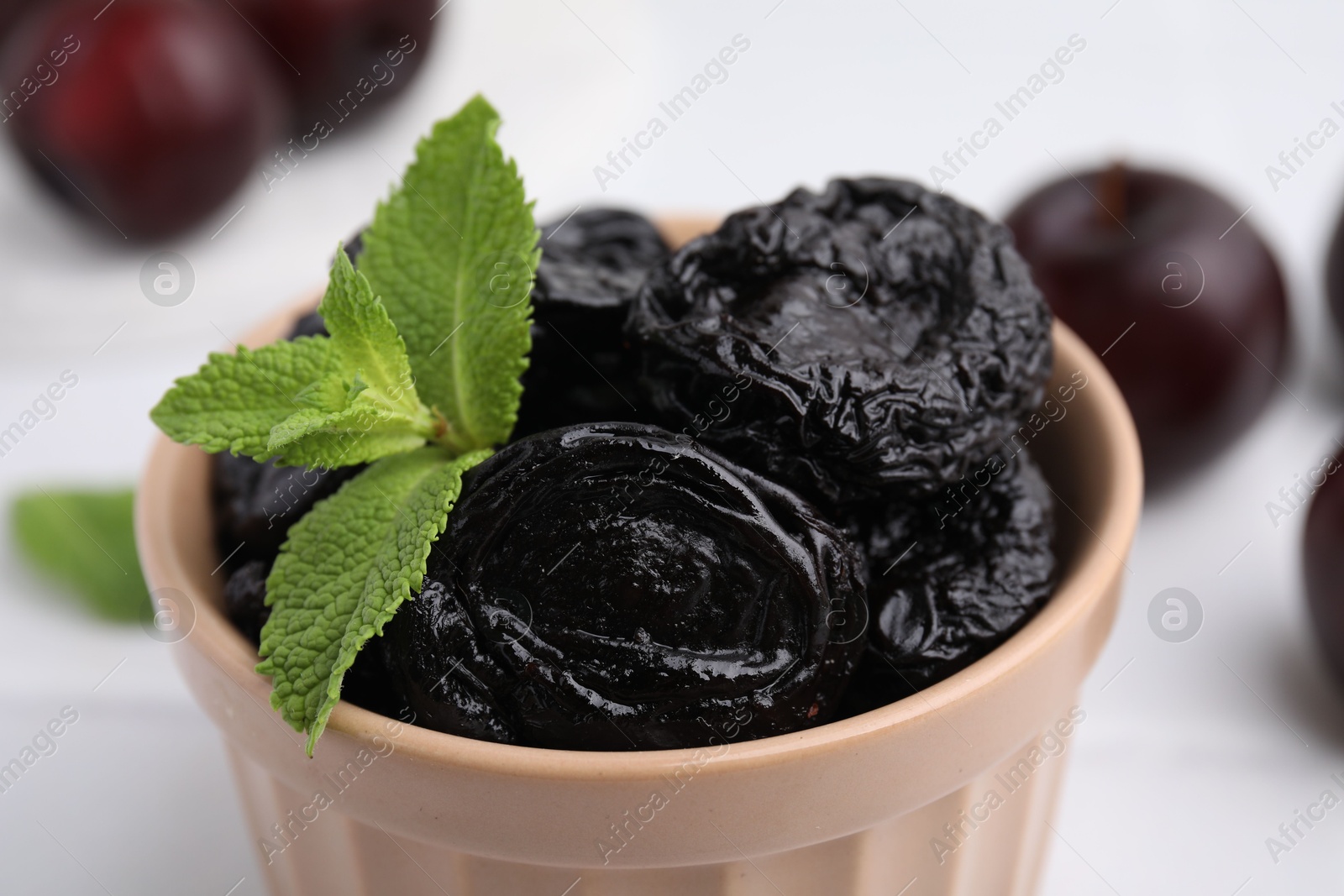 Photo of Tasty dried plums (prunes) and mint in bowl on white table, closeup