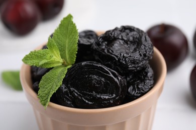 Tasty dried plums (prunes) and mint in bowl on white table, closeup