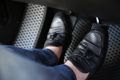 Photo of Man in black shoes pushing on pedal of car brake, closeup