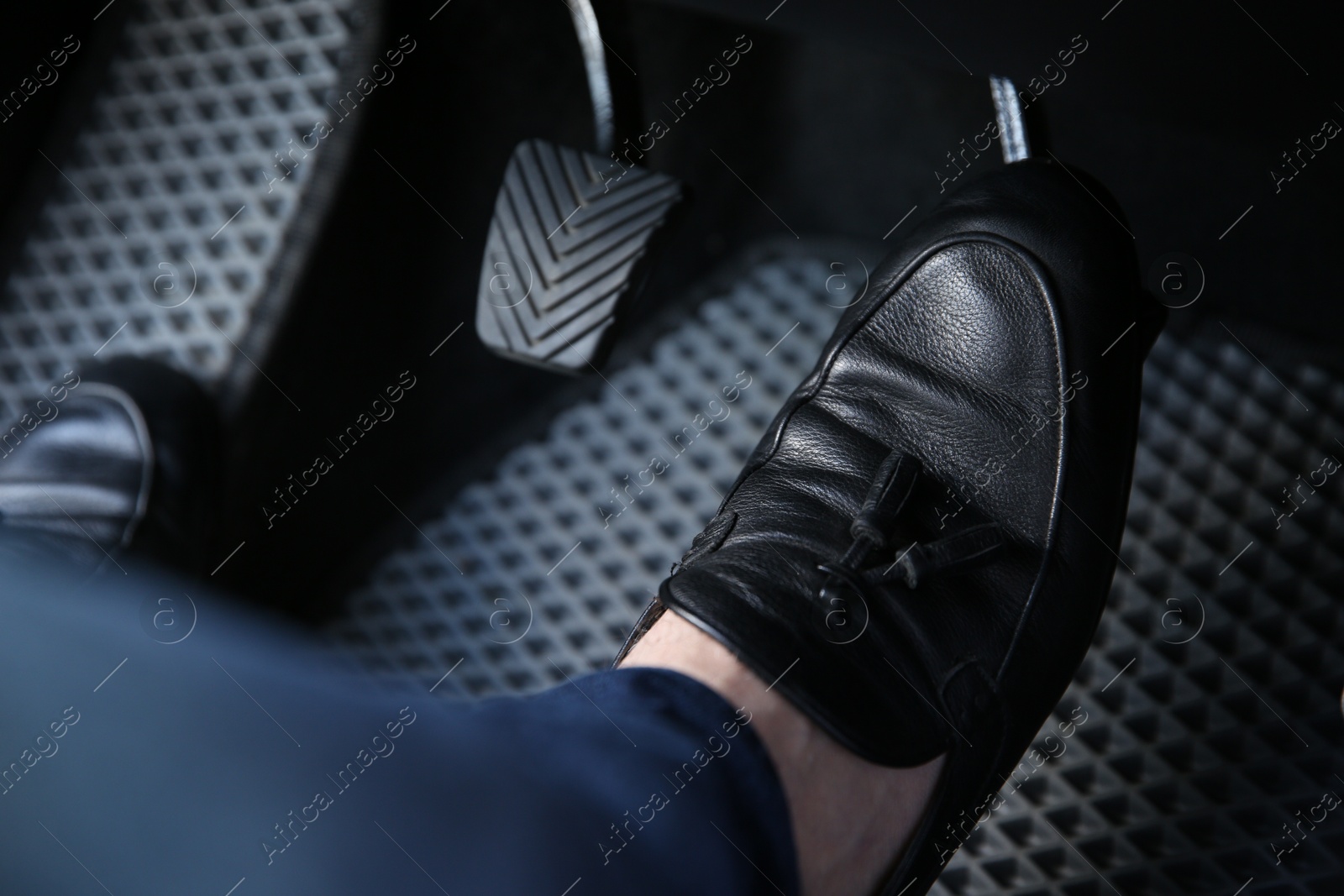 Photo of Man in black shoes pushing on pedal of car brake, closeup