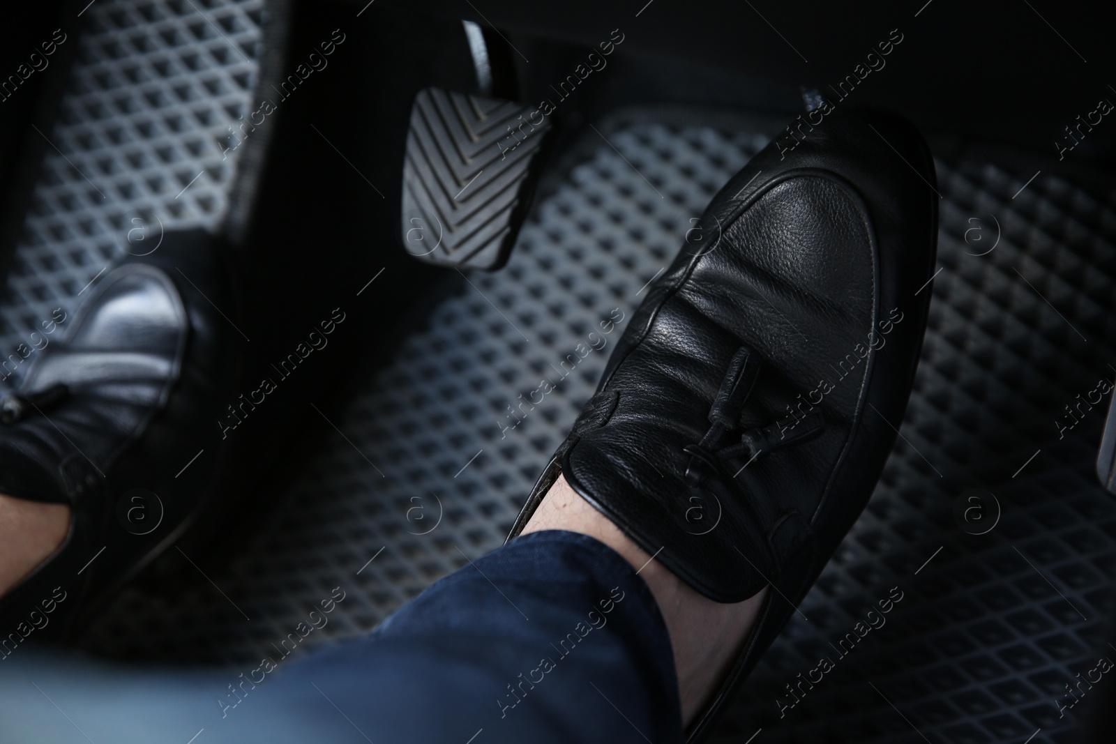 Photo of Man in black shoes pushing on pedal of car brake, closeup